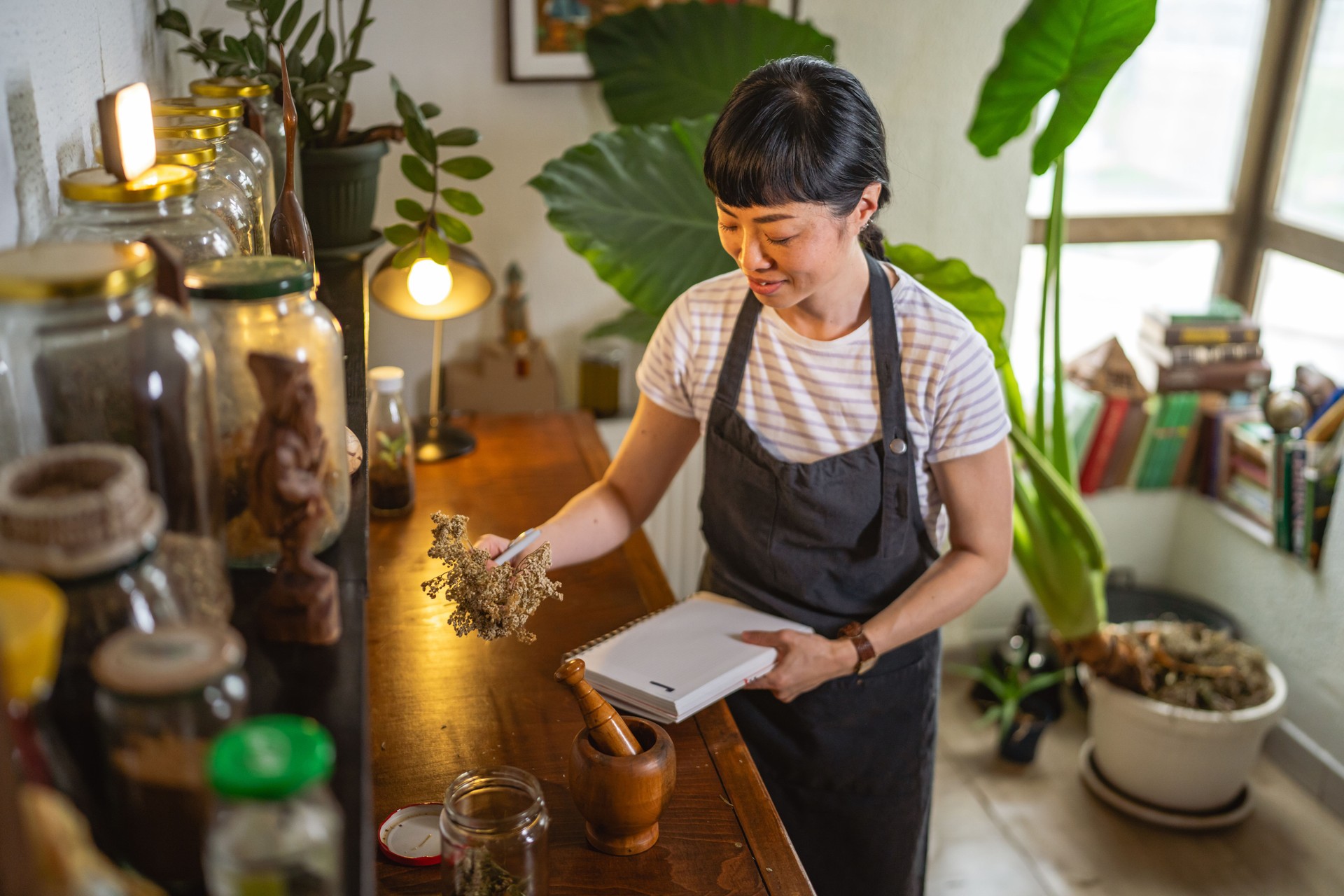 mature japanese woman and write recipes at notebook in herbal workshop